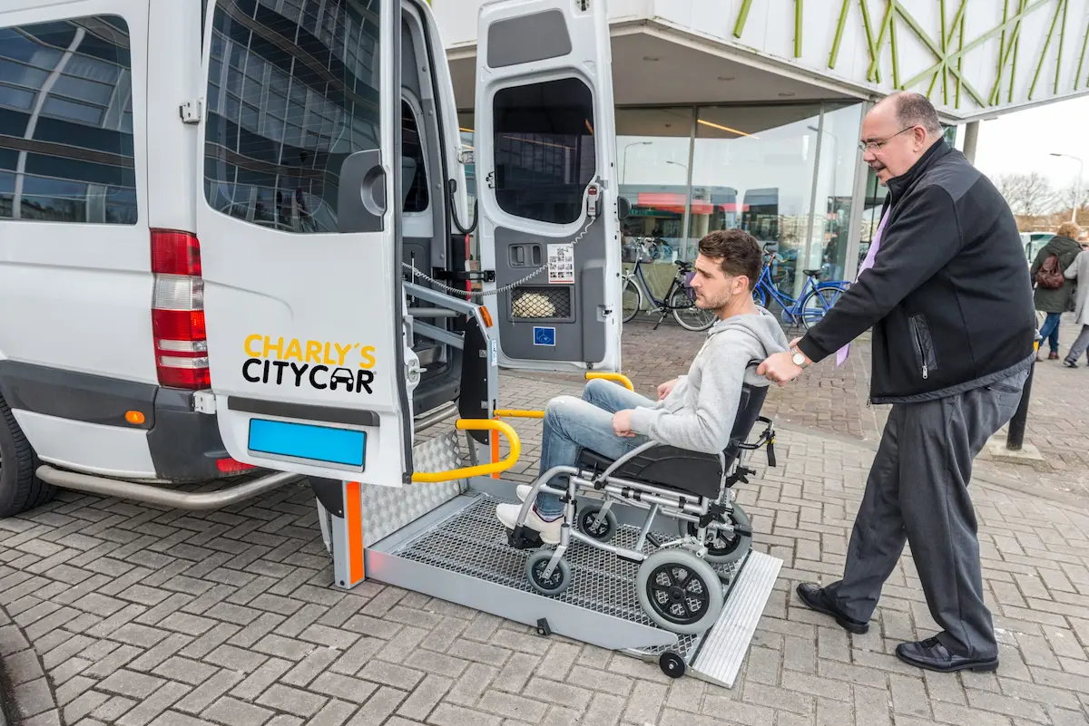 Ein Mann im Rollstuhl wird über eine Rampe in ein barrierefreies Fahrzeug von Charly´s Citycar® geschoben.
